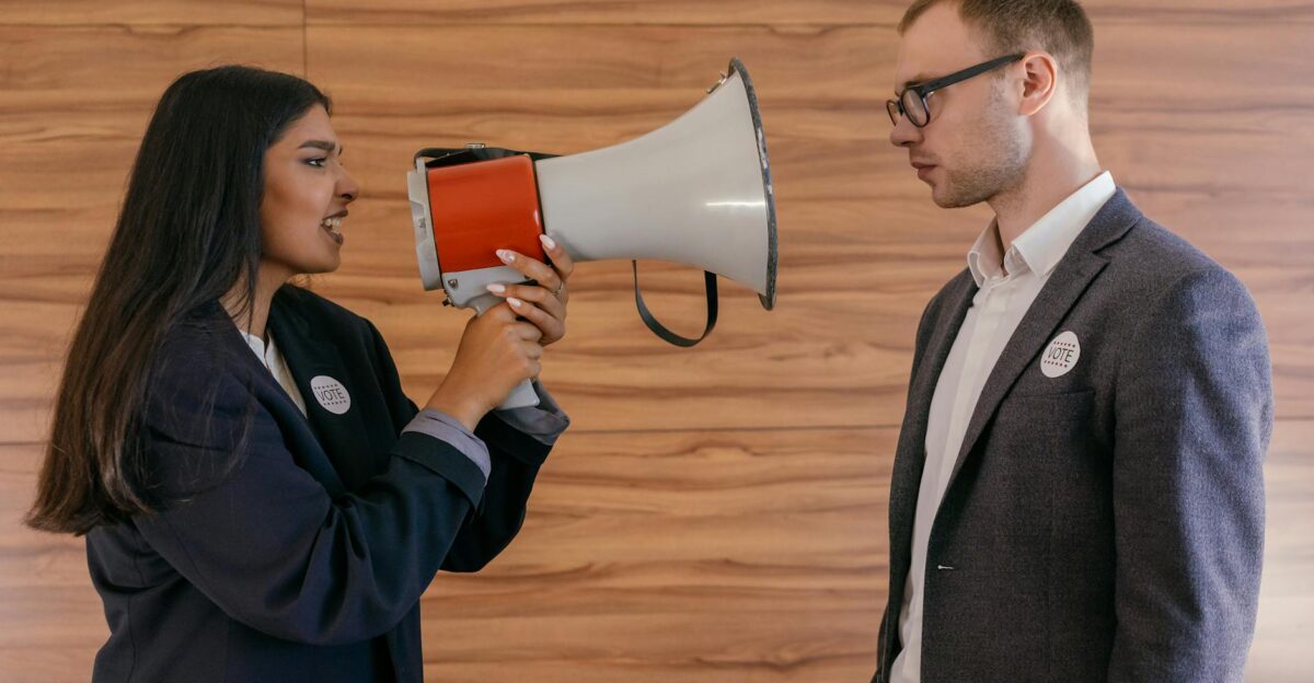 A woman using a megaphone to confront a man in a suit indoors symbolizing political debate