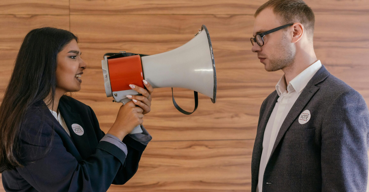 A woman using a megaphone to confront a man in a suit indoors, symbolizing political debate.