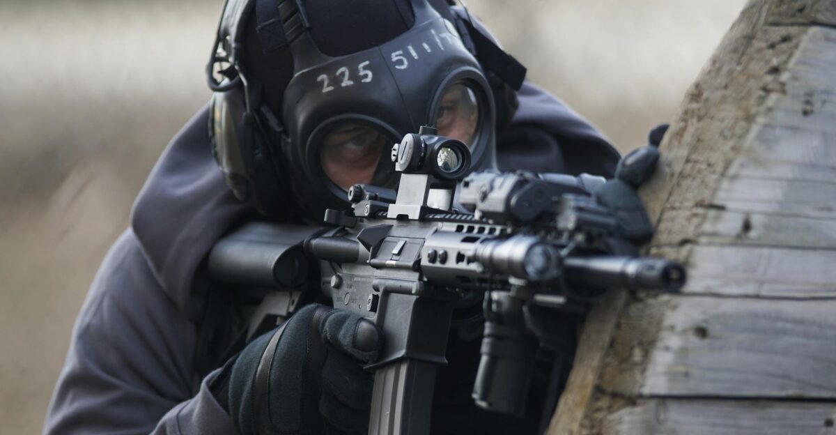 A tactical soldier in full gear aiming a rifle during an operation outdoors