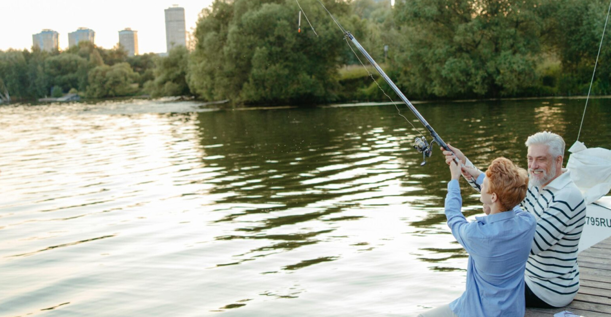 Senior man and young boy fishing together on a dock by a peaceful lake at sunset.
