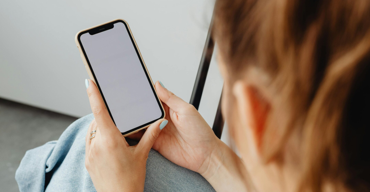 A woman holds a smartphone with a blank screen indoors, offering a mockup opportunity.