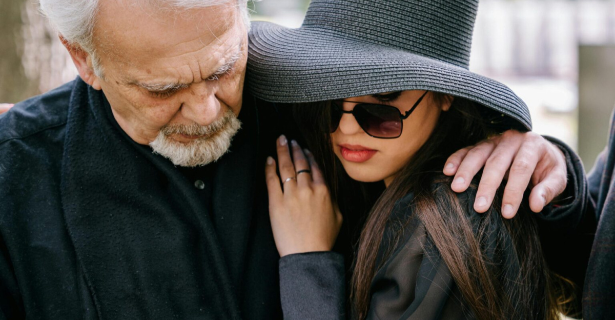 A group of adults in black clothing grieving together outdoors, conveying feelings of loss and sadness.