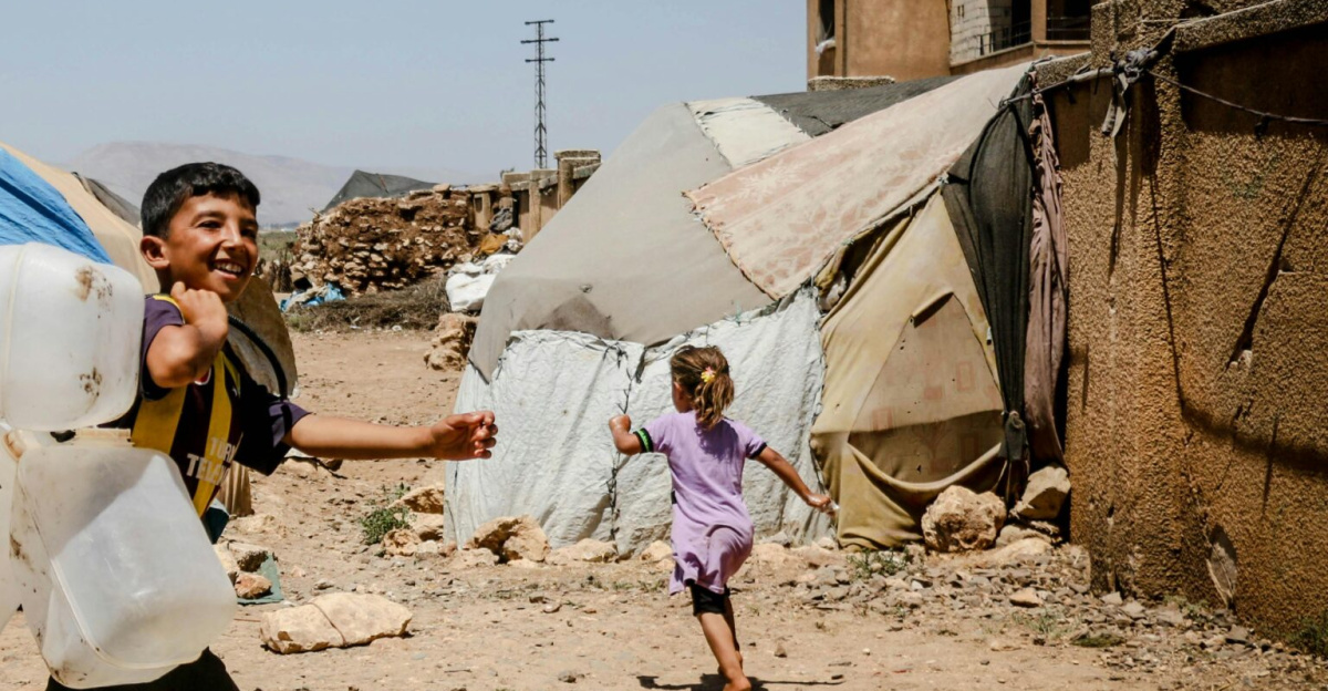Children in Idlib refugee camp carrying water jugs, smiling and walking.