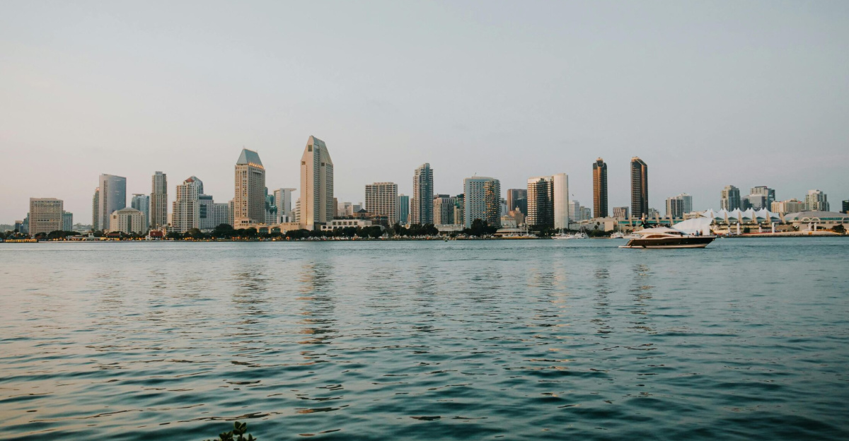 Panoramic view of San Diego skyline reflecting on the bay with a yacht cruising by.