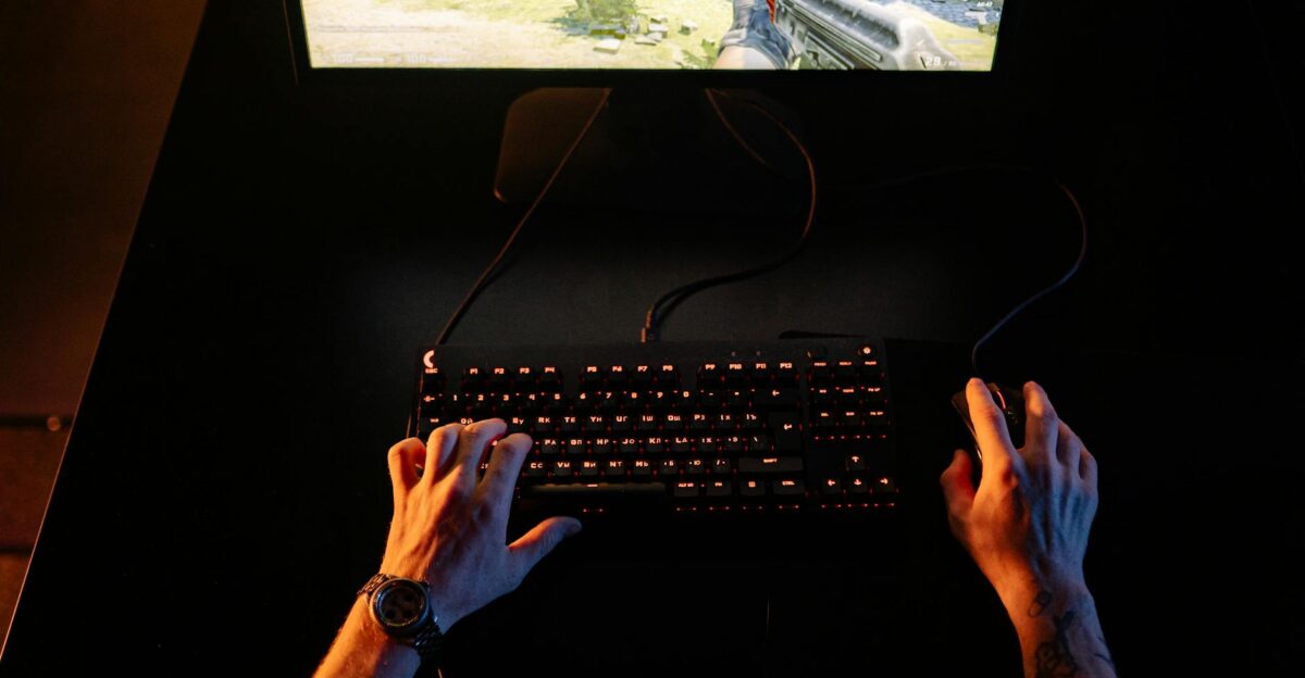 A gamer intensely playing a first-person shooter game on a computer setup indoors at night