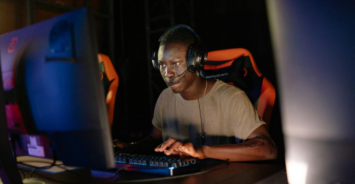 Young adult male intensely focused on computer gaming using headset and gaming keyboard indoors
