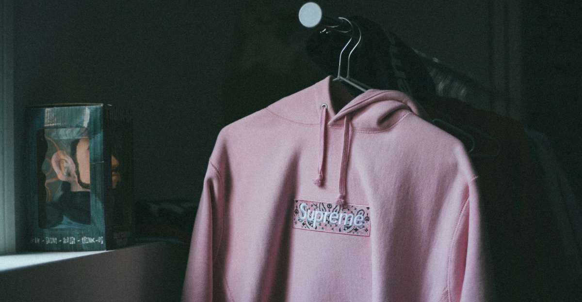 A pink hoodie hangs on a clothes rack in a dimly lit room with a boxed toy nearby.