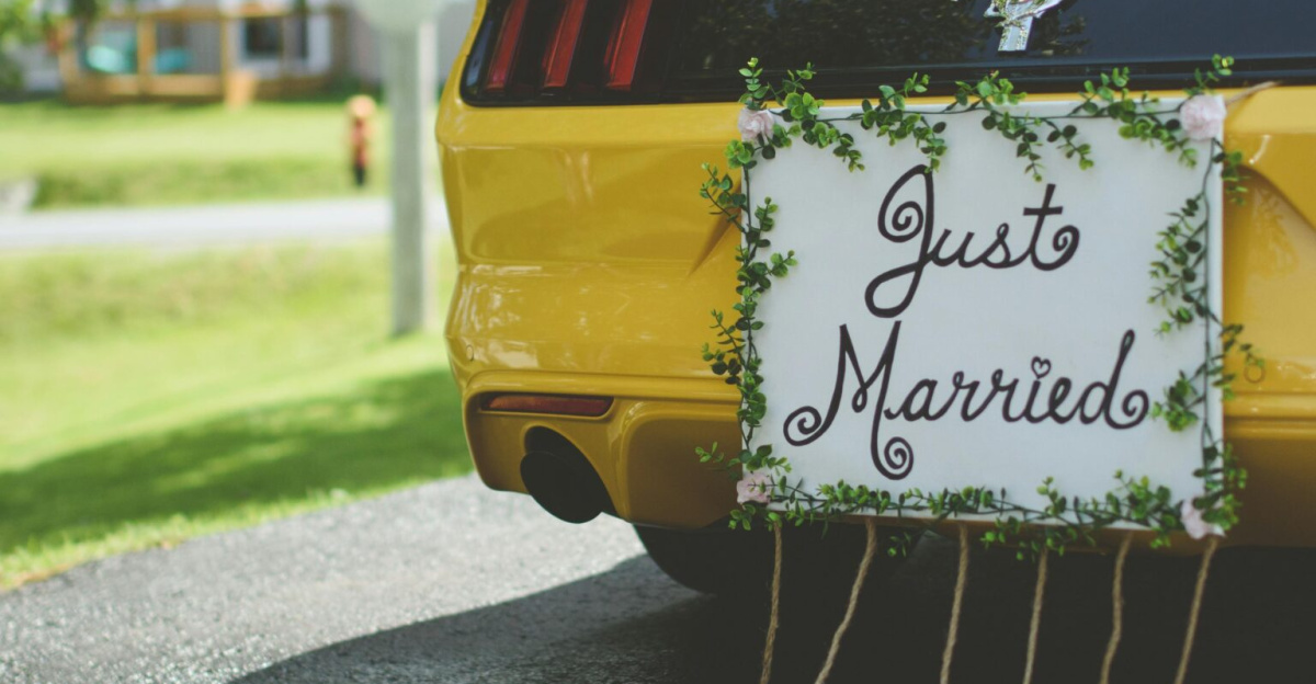 A vibrant yellow sportscar adorned with a Just Married sign and tin cans on a sunny day.