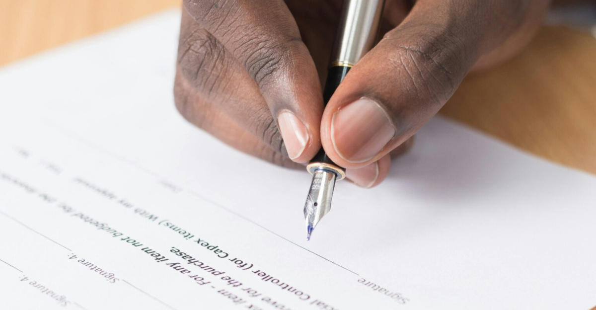 A hand holding a pen signing a document close-up on a desk, symbolizing agreement or contract finalization.