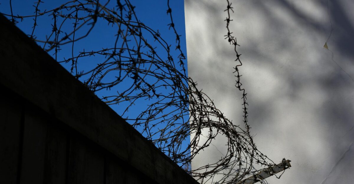 Barbed wire atop a concrete fence casting shadows symbolizing security and restriction