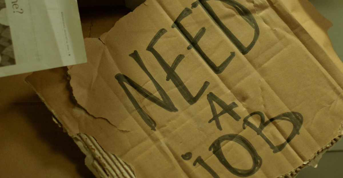 Close-up of a cardboard sign and newspaper depicting joblessness and unemployment.