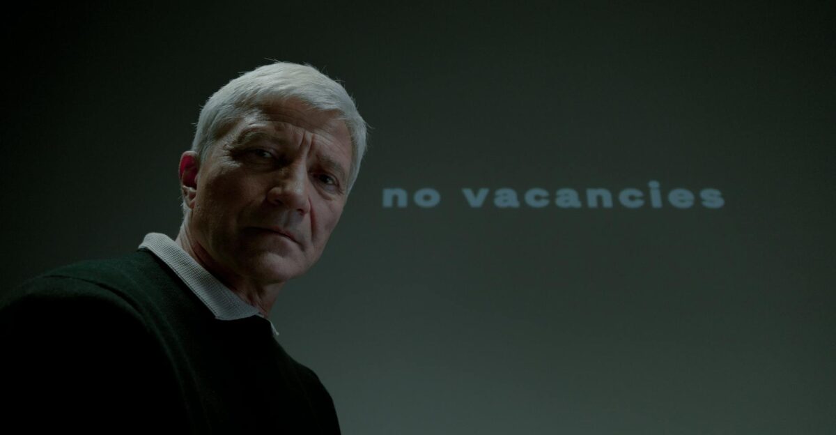 Senior man looks serious in front of a no vacancies message highlighting unemployment issues