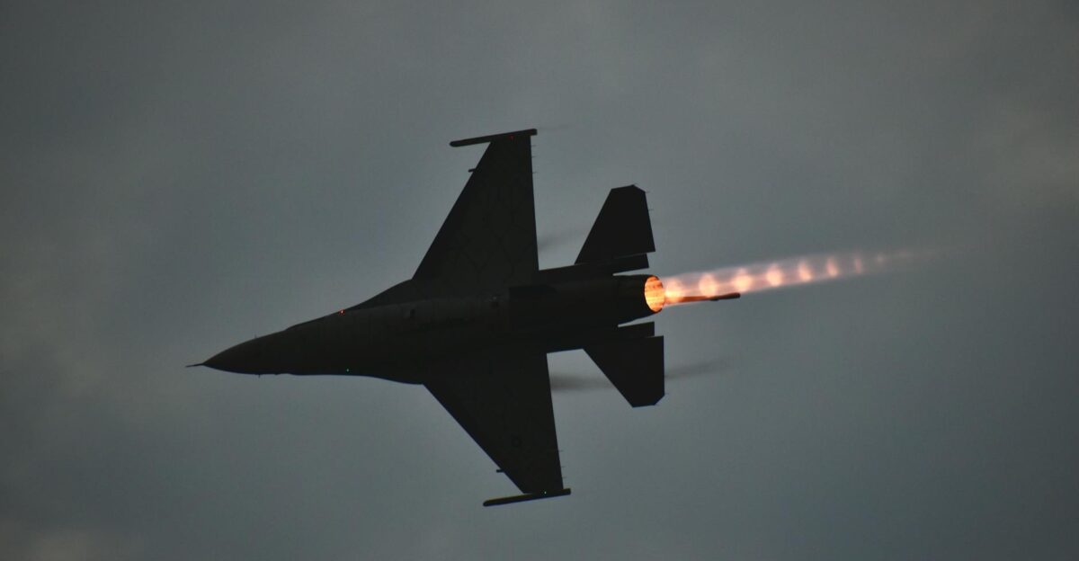 Dynamic F-16 jet showcasing an afterburner flame against a dusky sky