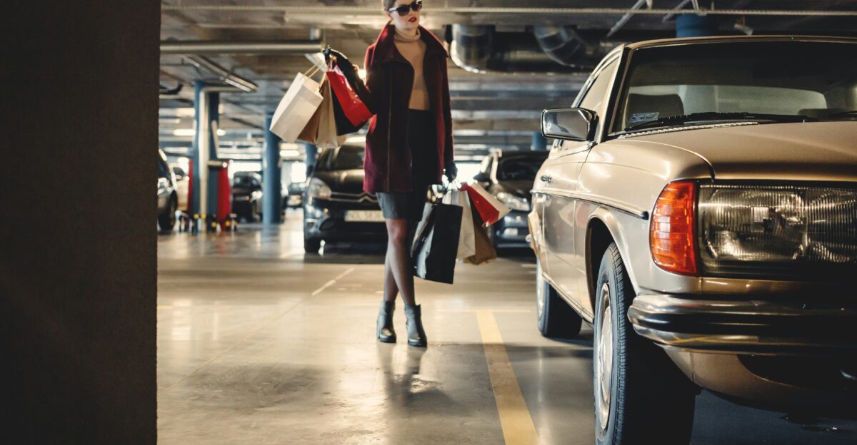 woman carrying shopping paper bags walking towards beige car inside parking lot