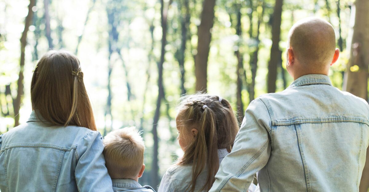 man and woman holding hands together with boy and girl looking at green trees during day