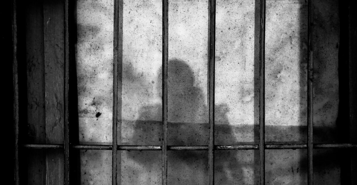 a shadow of a person behind bars in a jail cell