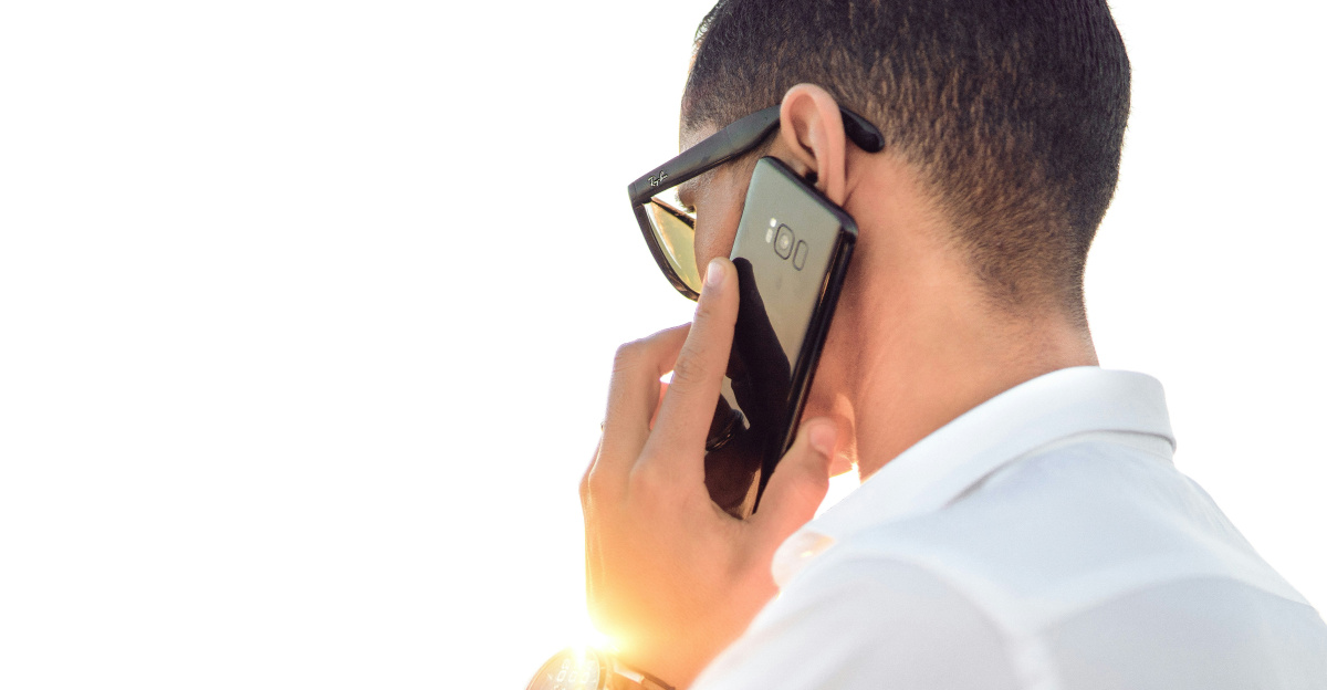 man holding smartphone standing in front of calm body of water