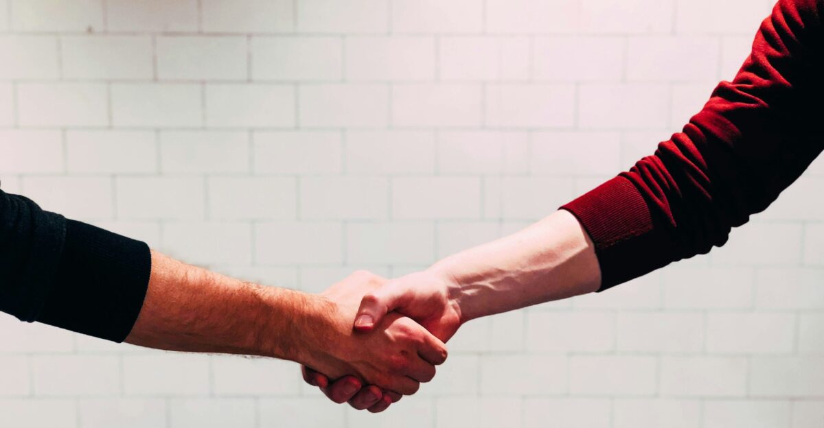 two person shaking hands near white painted wall