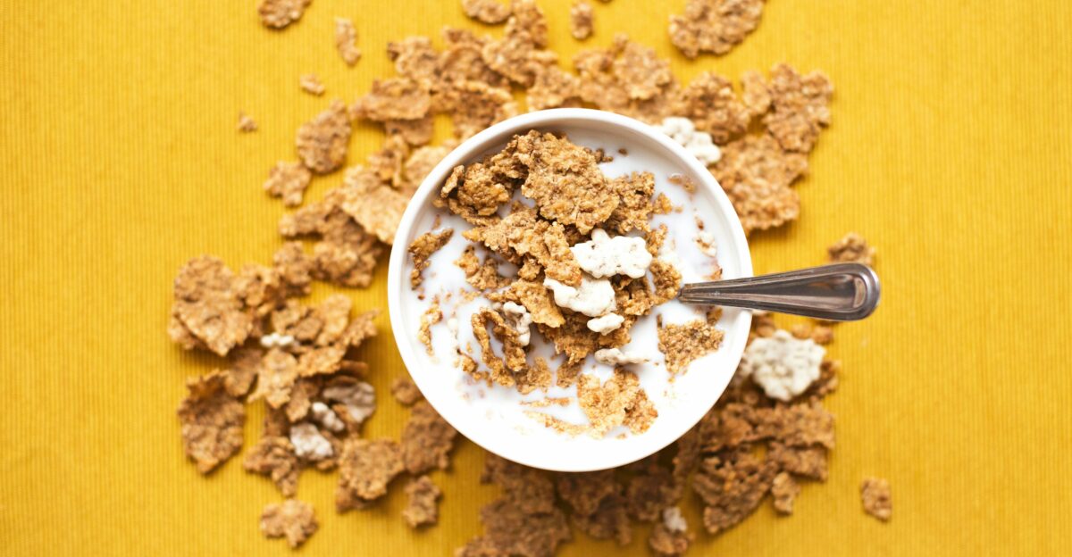 top view of corn flakes in bowl with milk and silver spoon