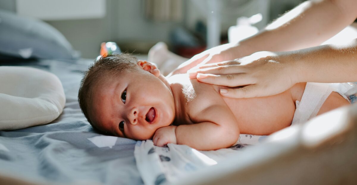 baby laying on bed while woman massaging his back
