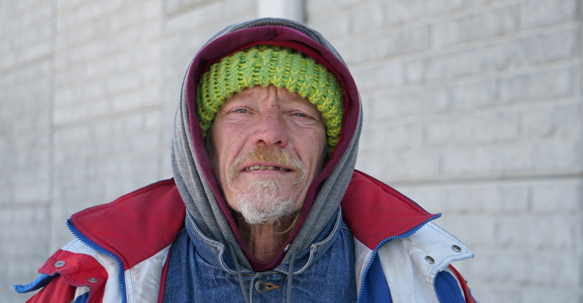 smiling man wearing hooded jacket near gray concrete wall