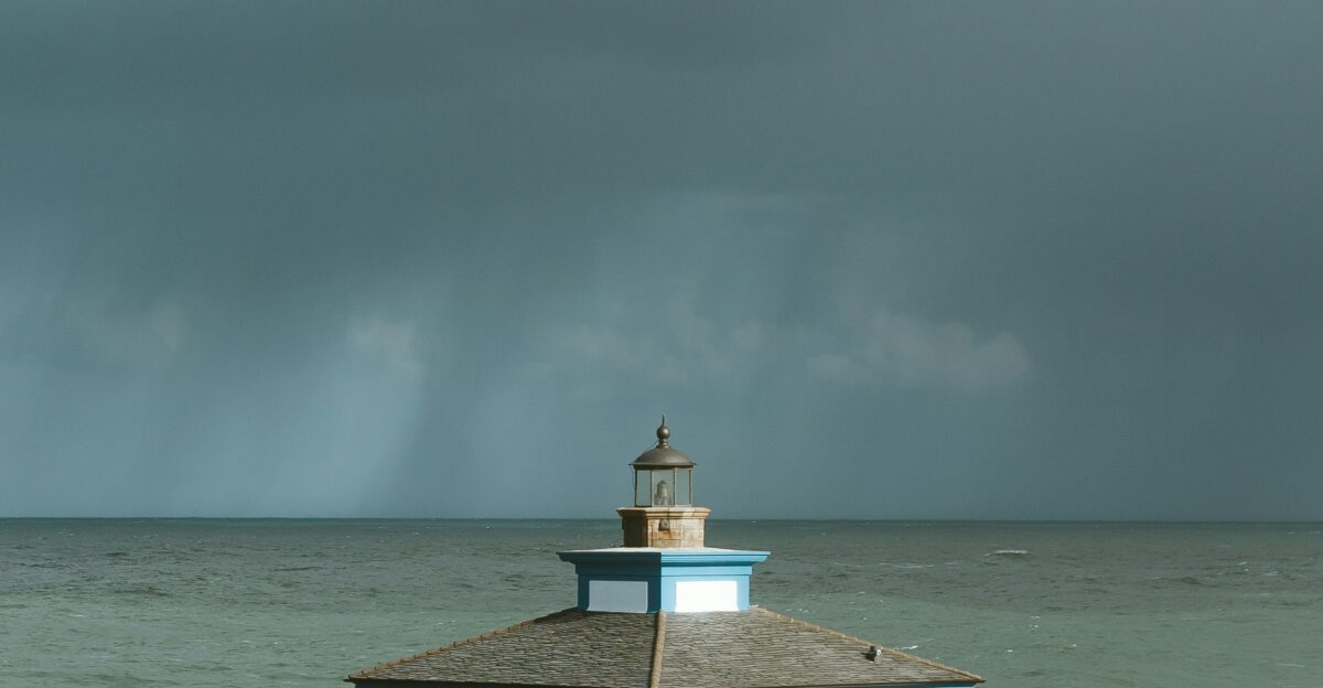 white and blue concrete house on hill near body of water under cloudy sky
