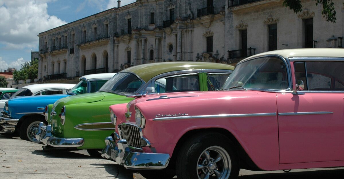 pink and green vintage car parked beside brown concrete building during daytime