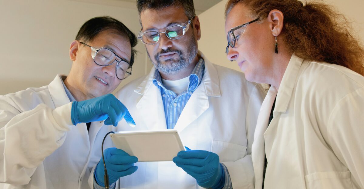three people in lab coats looking at a tablet