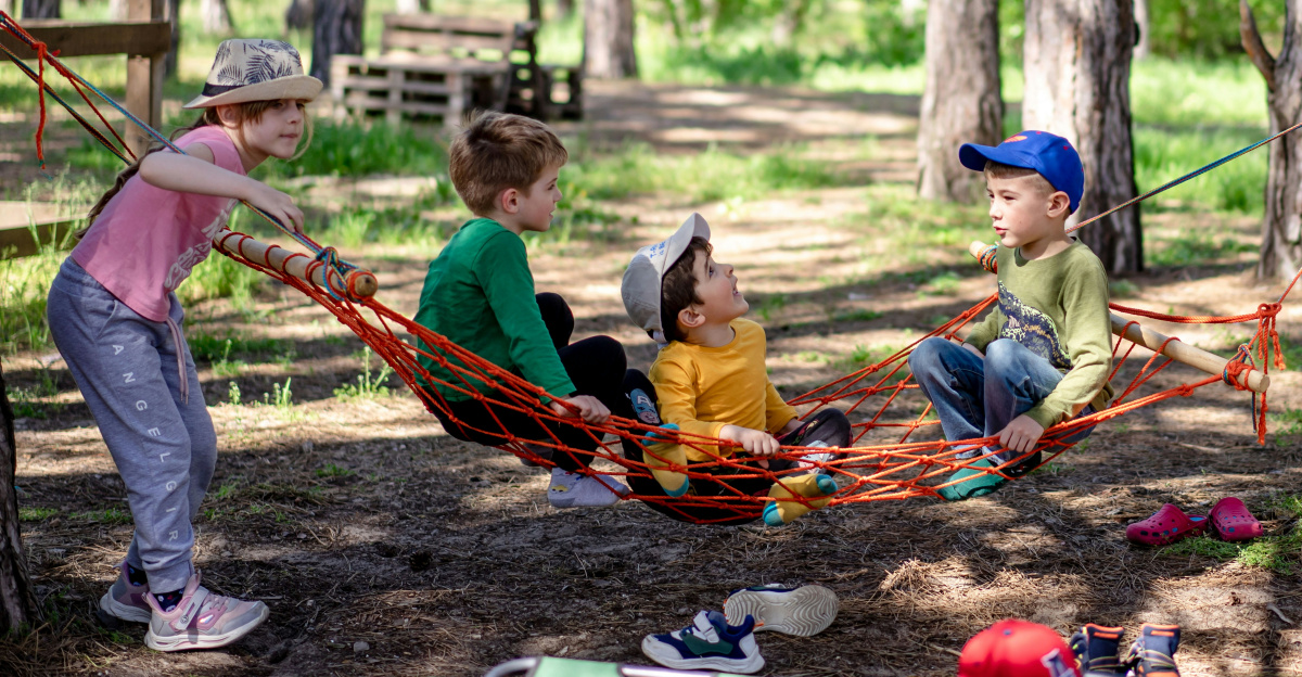 a group of kids sitting in a hammock in the woods