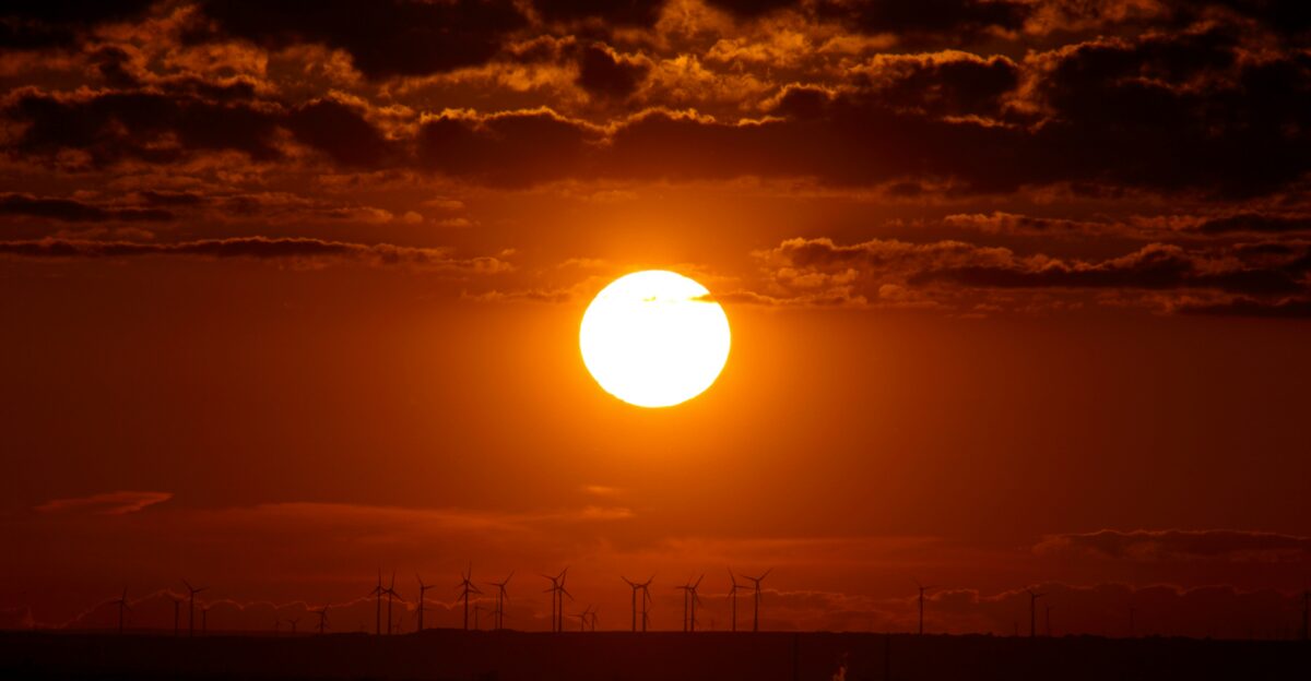 the sun is setting over a wind farm