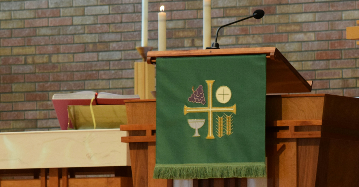 a priest standing at a podium in front of a brick wall