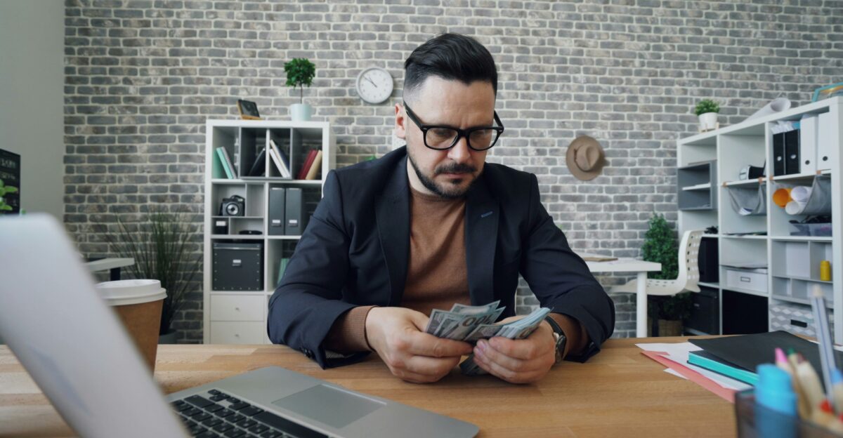 a man sitting at a table with a laptop and money
