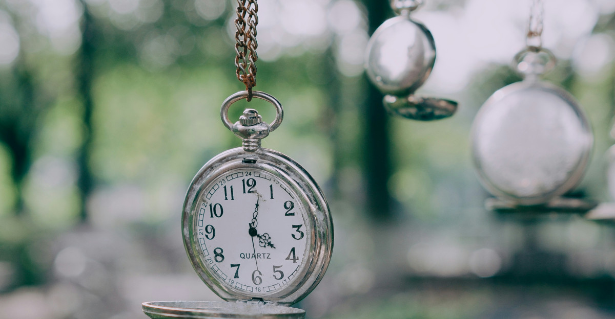 A clock hanging from a chain in a forest