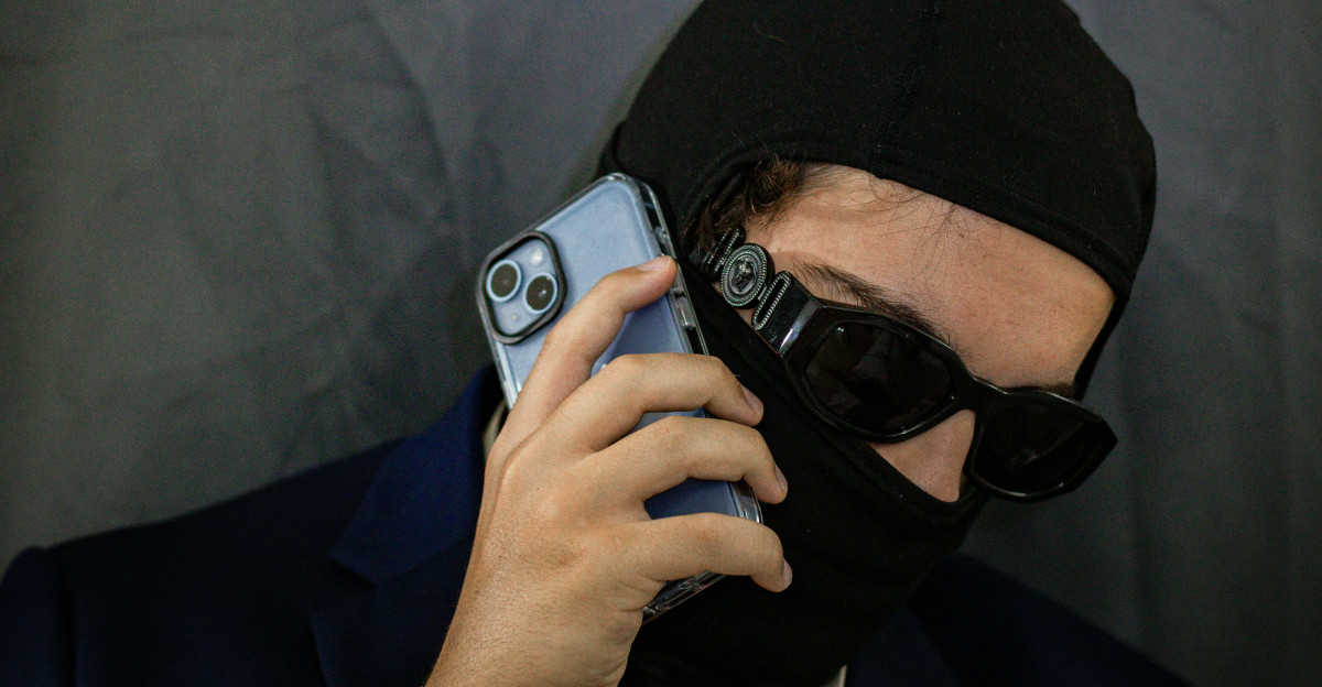 A man wearing a black mask holding a cell phone