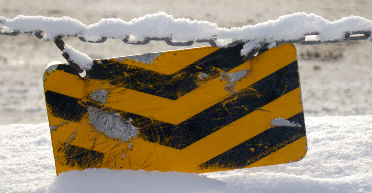 A yellow and black sign sitting on top of snow covered ground