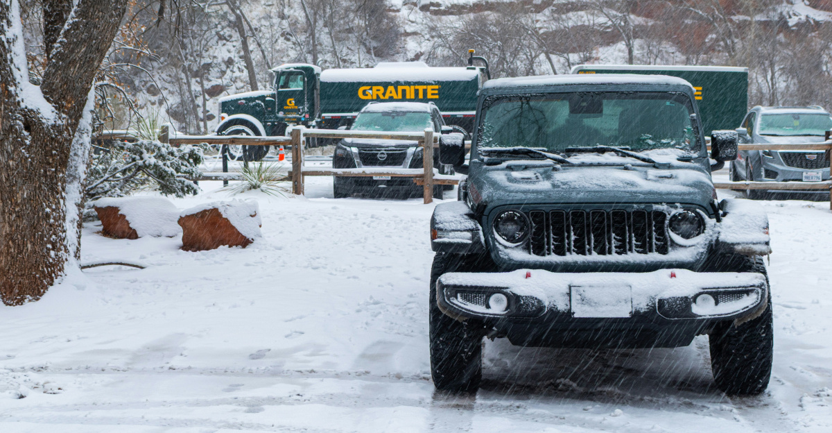 Dark jeep parked in snowy lot with trucks