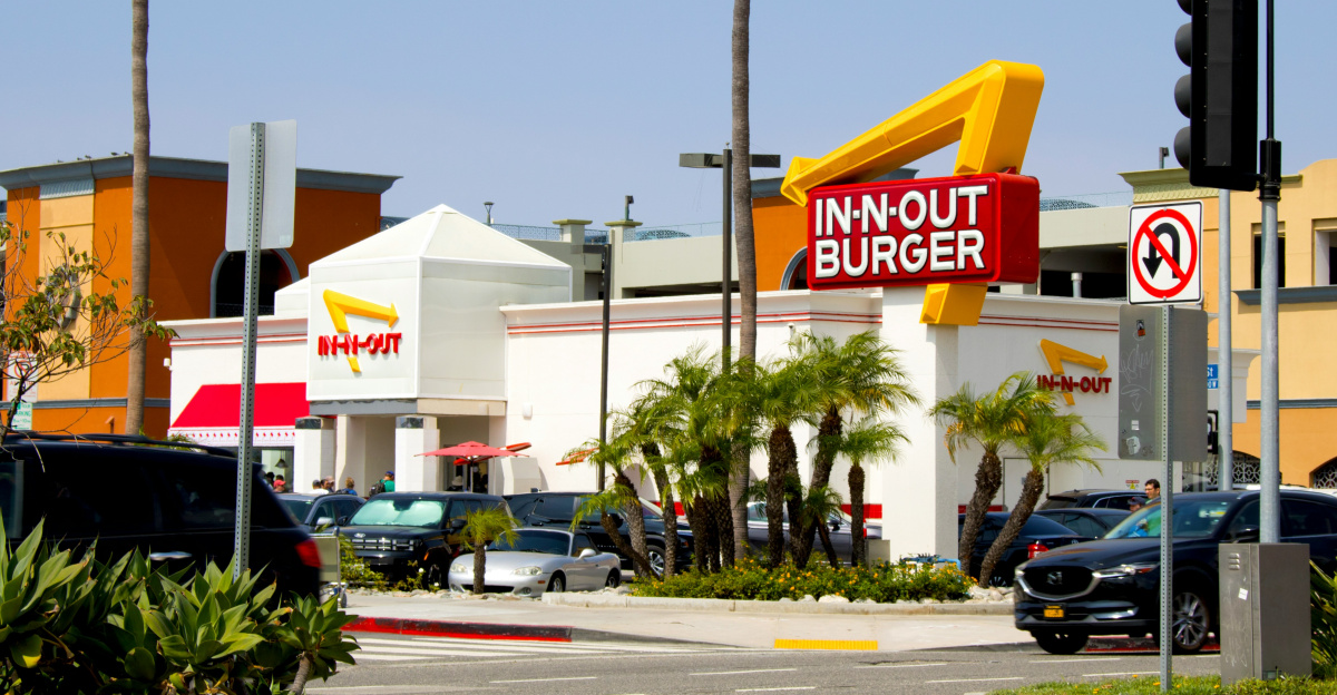 In-n-out burger restaurant with palm trees and cars.
