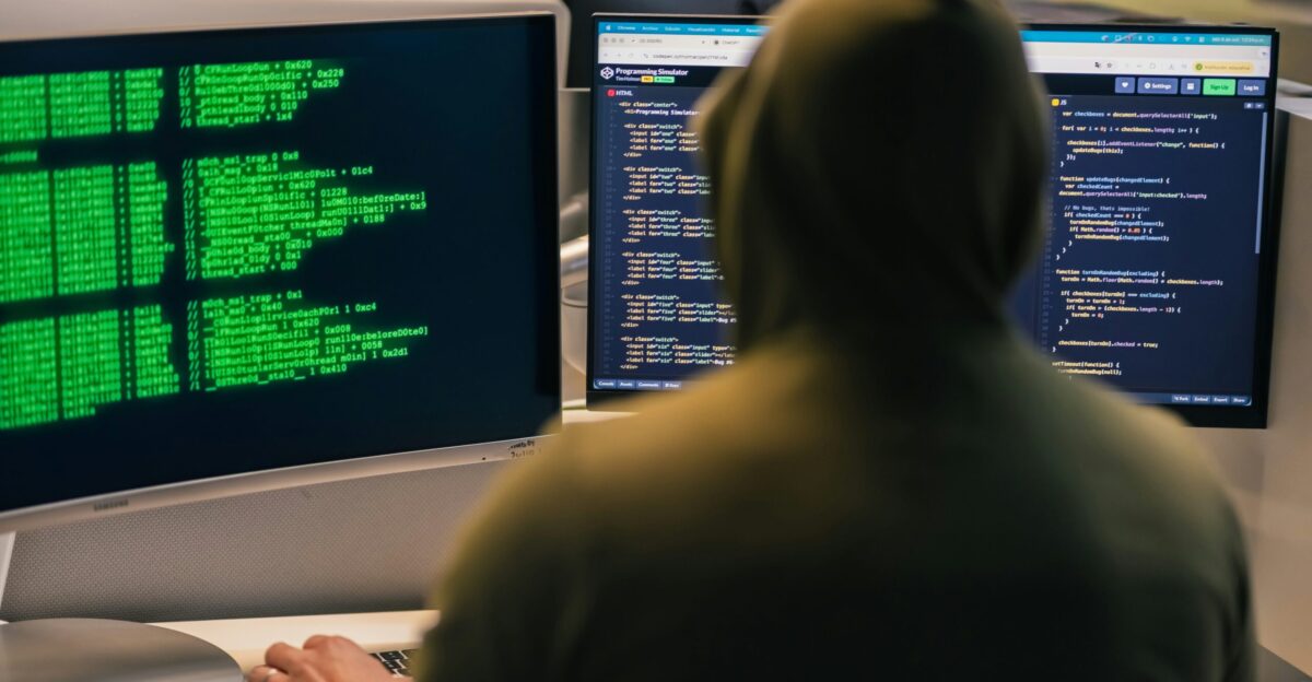 Hacker in hoodie working on multiple computer screens