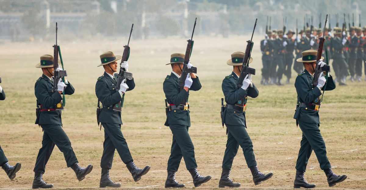 Soldiers in uniform marching with rifles on a field.