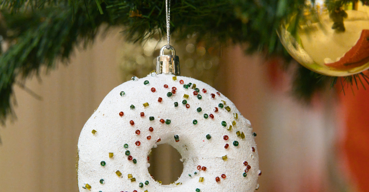 A donut ornament hangs on a christmas tree.
