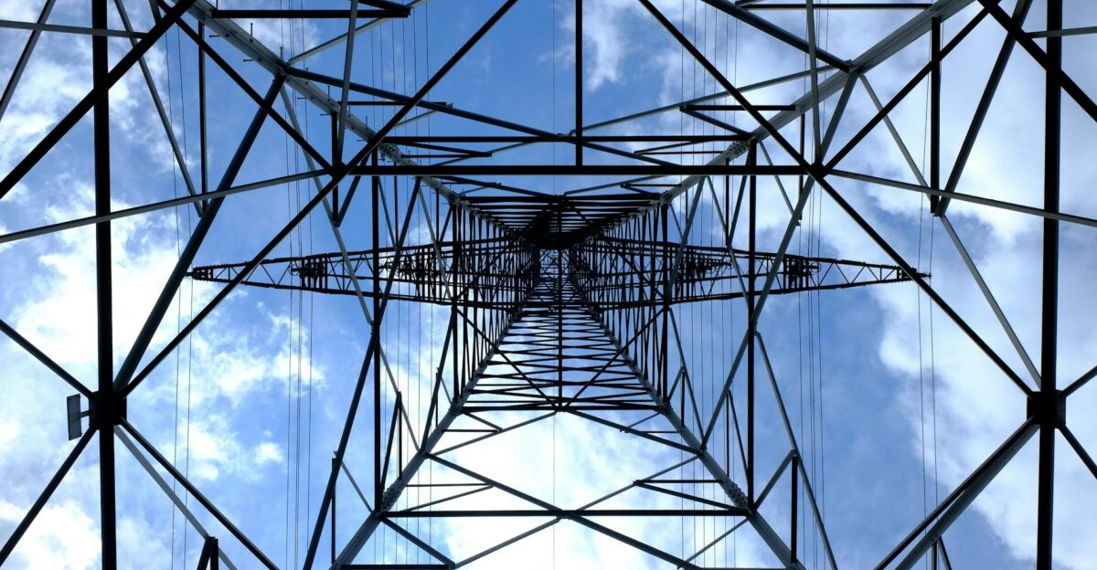 Looking up at a steel power pylon against a bright blue sky