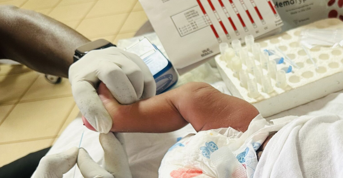The image shows a baby lying comfortably on a bed at the Tamale Teaching Hospital recovery room. The setting includes screening items used for testing a neonate shortly after birth. The scene conveys feelings of comfort and tranquility as the newborn rests peacefully under a cot-sheet