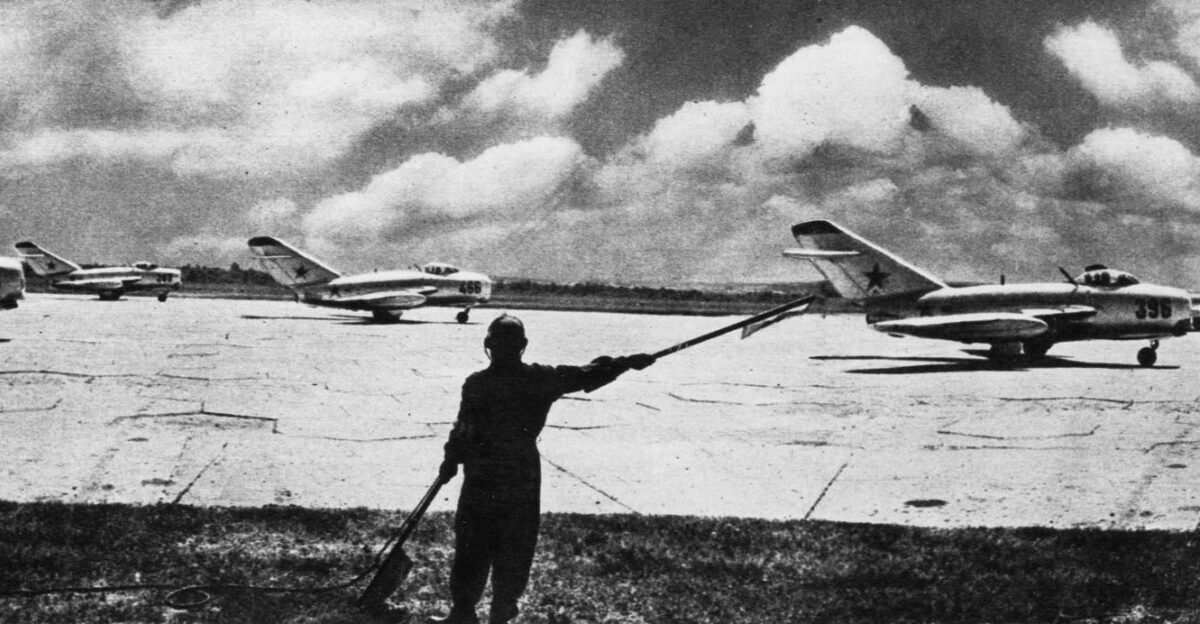 A flight of Soviet Mikoyan-Gurevich MiG-15 jet fighters prepares to take off under direction of a field controller equipped with flags and radio