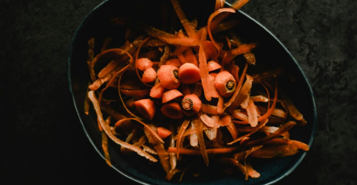 Close-up photo of fresh carrot peels and scraps in a dark bowl perfect for food waste or preparation themes