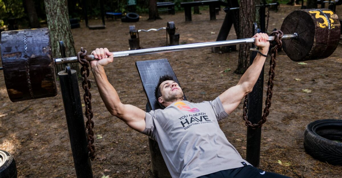 Man weightlifting outdoors using a bench press setup amid trees for strength training