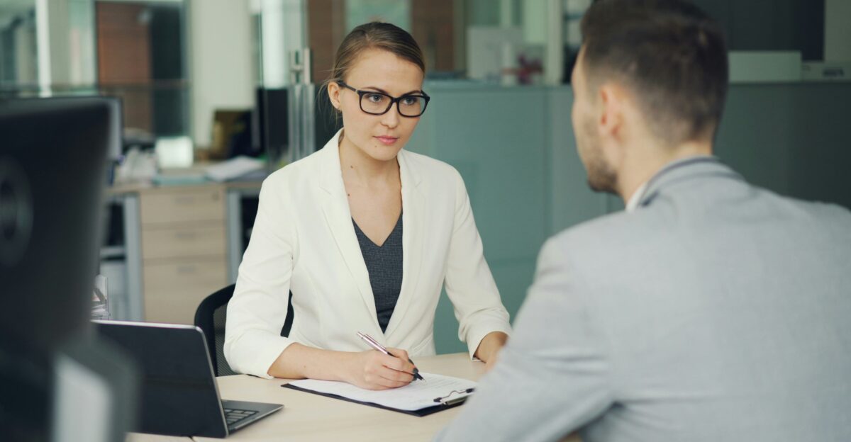 Woman in glasses interviews man at office desk