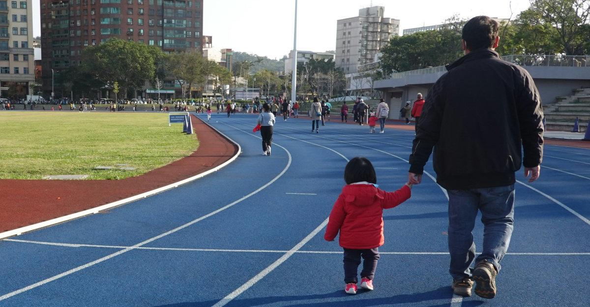 Man and child walking on a blue running track.